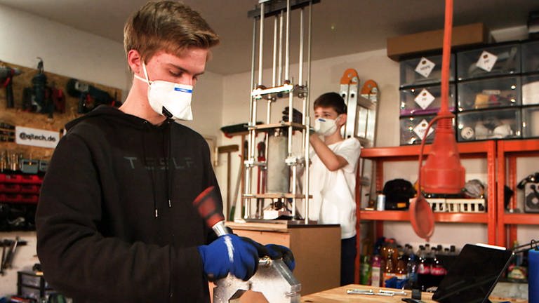 Zwei junge Schüler mit Atemmasken bauen an Maschinen aus Plastikmüll Schutzvisiere für Krankenhäuser