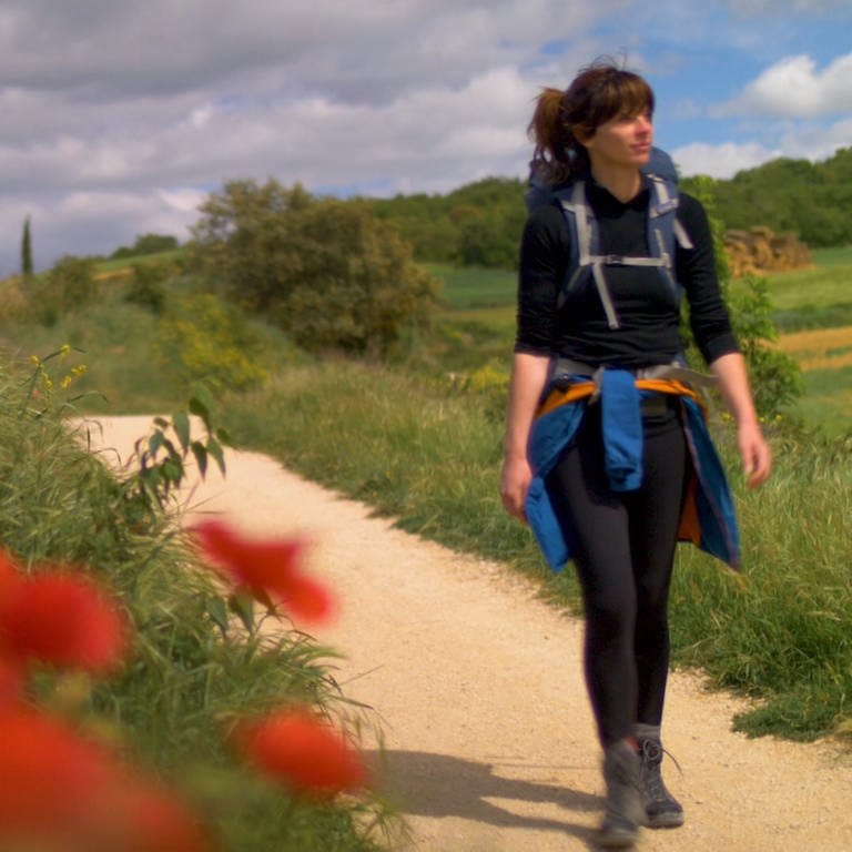 Frau mit Rucksack wandert auf Feldweg, der von roten Mohnblumen gesäumt ist (Foto: SWR)