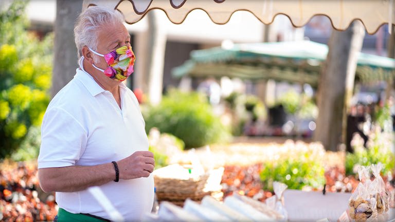 : Älterer Mann mit grauen Haaren und einer bunten Maske vor seinem Stand auf dem Mainzer Wochenmarkt  (Foto: SWR)