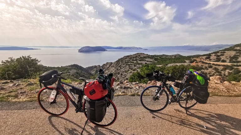 Zwei Fahrräder bepackt mit vielen Taschen und im Hintergrund zwei kroatische Inseln. 