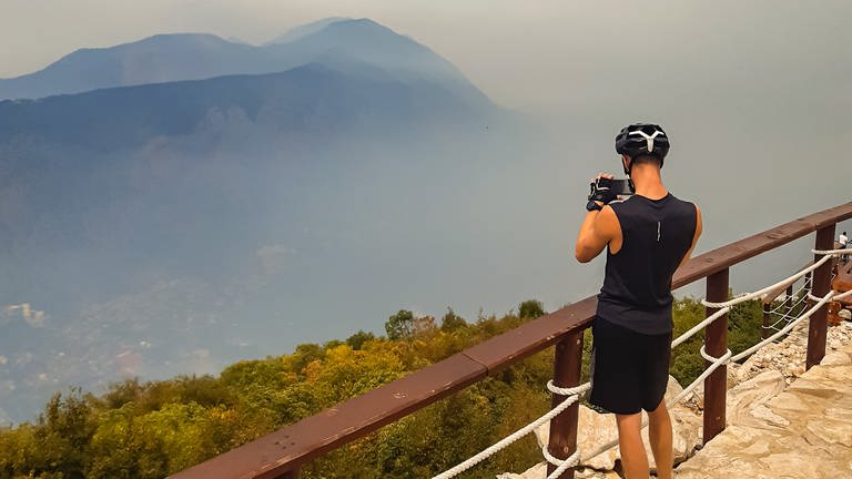 Junger Mann, der an einem Aussichtspunkt in den Bergen ein Foto macht.