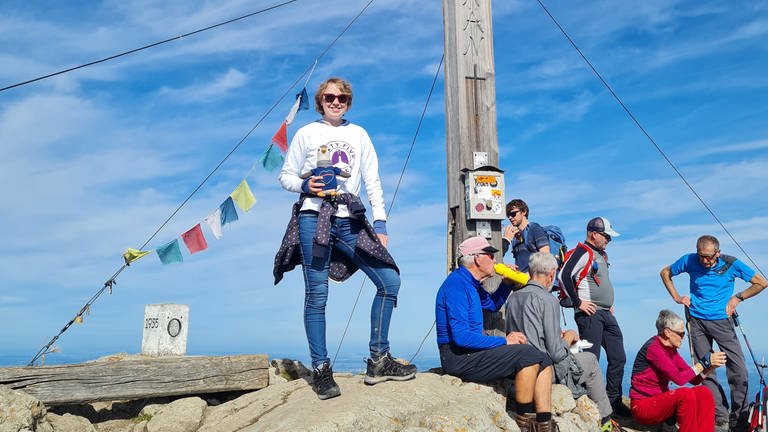 Junge Frau steht neben einem Gipfelkreuz.