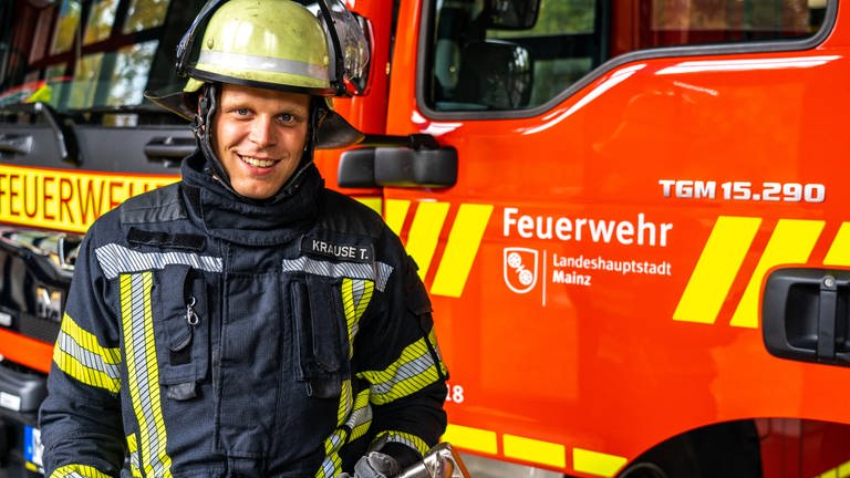 Junger Mann in Feuerwehrmontur vor einem Feuerwehrauto der Mainzer Berufsfeuerwehr (Foto: SWR)