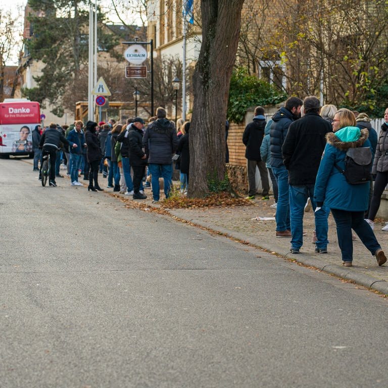 Menschen stehen in einer Reihe, ganz am Ende der Schlange sieht man den roten Impfbus. (Foto: SWR)