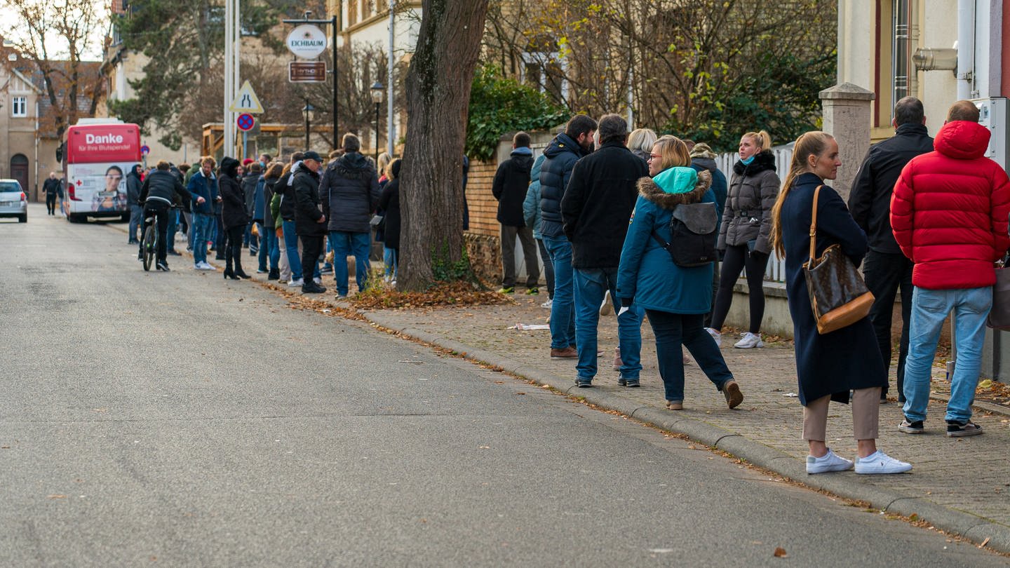 Menschen stehen in einer Reihe, ganz am Ende der Schlange sieht man den roten Impfbus. (Foto: SWR)