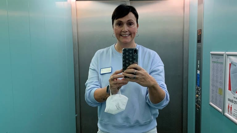 Frau in Pflegekleidung macht ein Selfie in einem Aufzug.