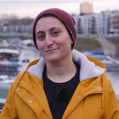 Porträt: Junge türkischstämmige Frau mit Mütze und gelbem Regenmantel