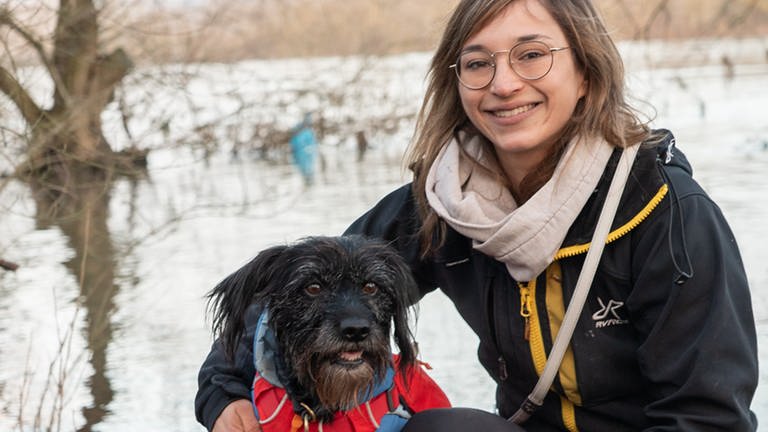 Hund und Frau mit Brille lächeln vor Fluss. (Foto: SWR)