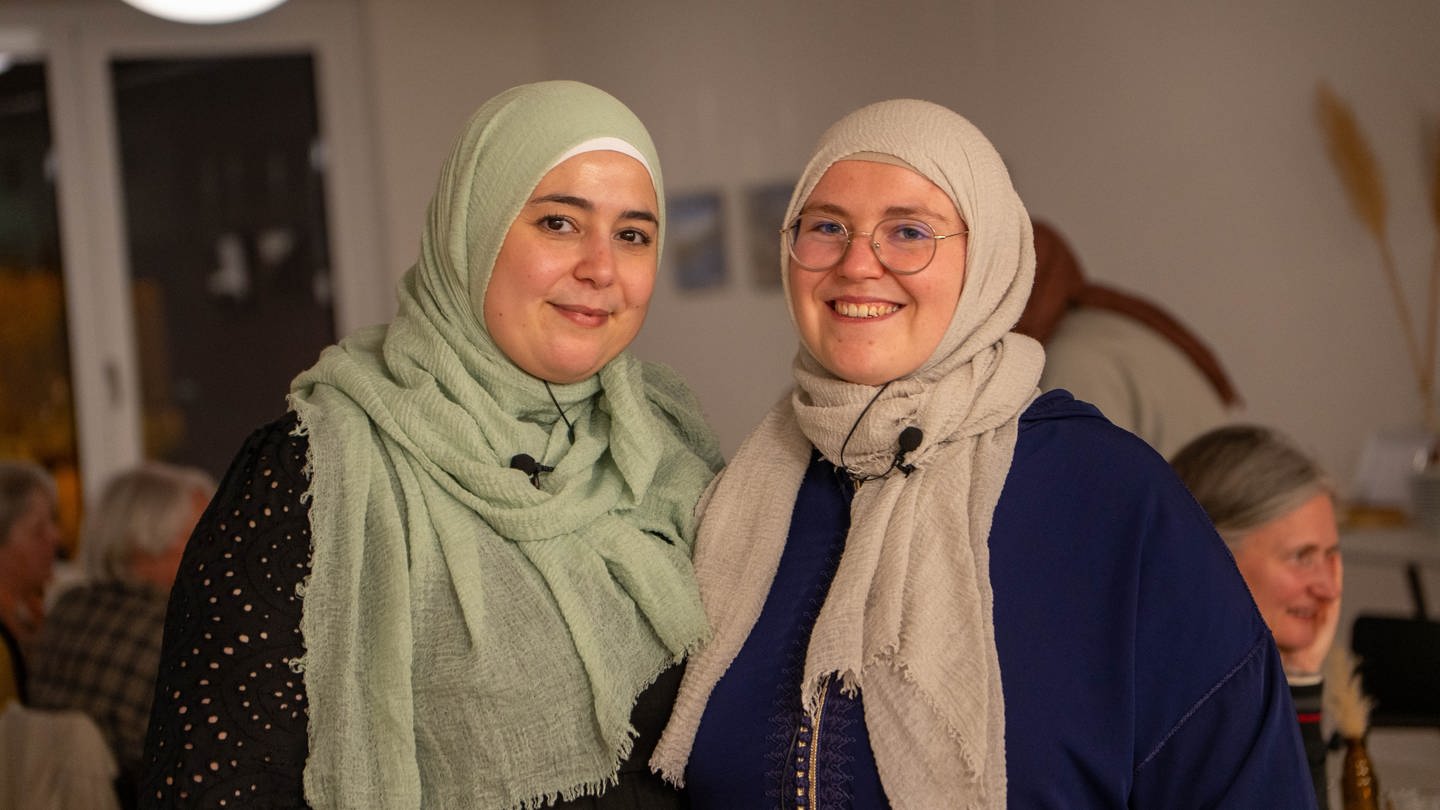 Zwei Frauen mit Kopftüchern lächeln in die Kamera.