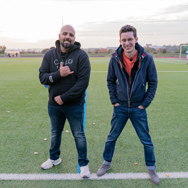 Zwei junge Männer in Freizeitkleidung auf einem Fußballplatz