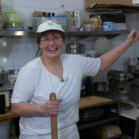 Frau mit Brille, kurzen Haaren und weißer Mütze und T-Shirt steht am Ofen in der Bäckerei (Foto: SWR)
