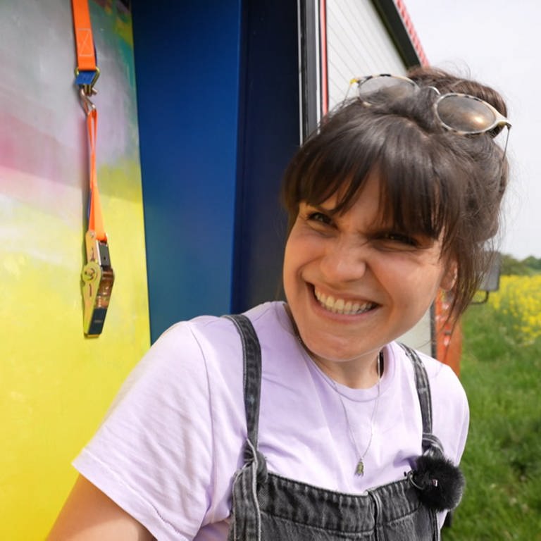 Junge Frau in Latzhose vor einem Gemälde in ihrem VW-Bus