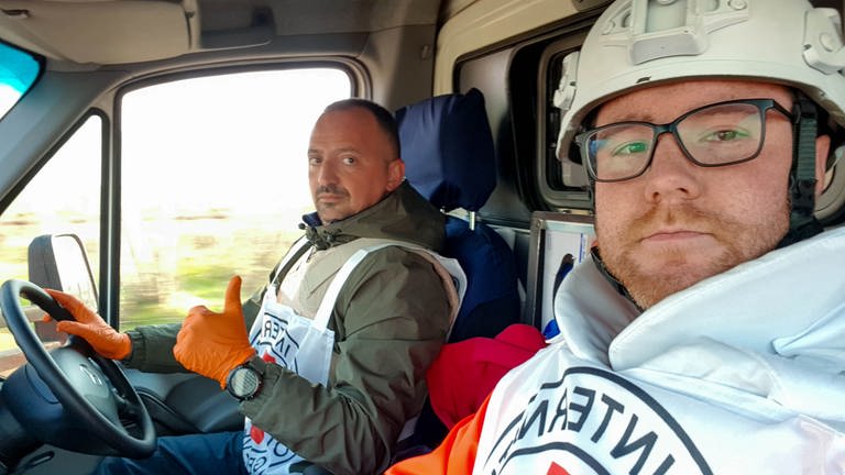 Rouven und sein israelischer Kollege sitzen mit Westen vom Roten Kreuz in einem Rettungswagen. Sie waren im ukrainischen Kriegsgebiet im Einsatz. (Foto: SWR, 0)