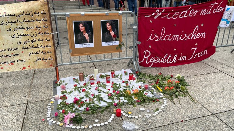 Unter zwei Fotos von Mahsa Amini formen Teelichter ein Herz. Darin liegen Rosen und Kerzen. Die Demo für Freiheit im Iran fand in Mainz statt. (Foto: SWR, Damaris Diener)