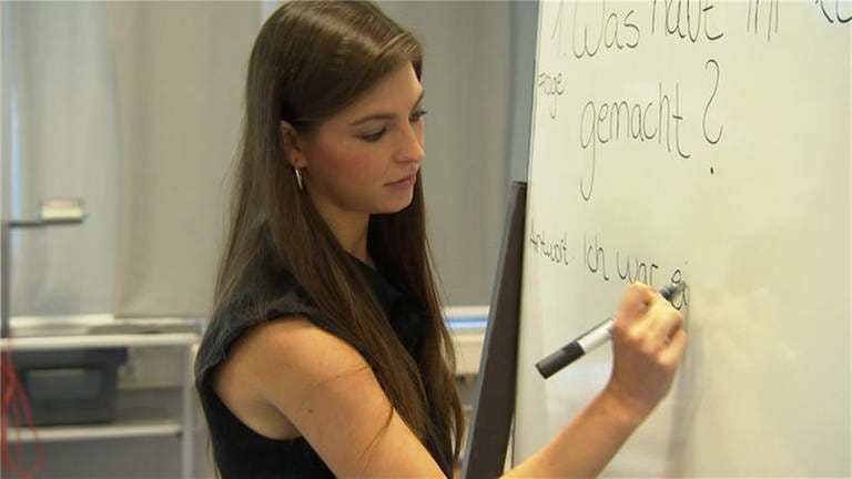 Junge Frau mit braunen Haaren schreibt auf Whiteboard.