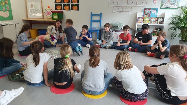 Kinder sitzen in einem Kreis auf dem Boden.