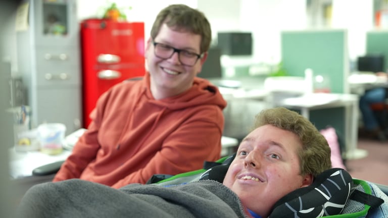 Zwei junge Männer – einer liegend, einer sitzend – arbeiten in einer Behindertenwerkstatt