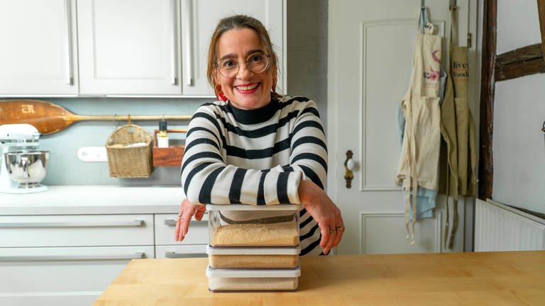 Junge Frau mit Brille und gestreiftem Pullover lehnt über einem Stapel von Büchern in der Küche (Foto: SWR)