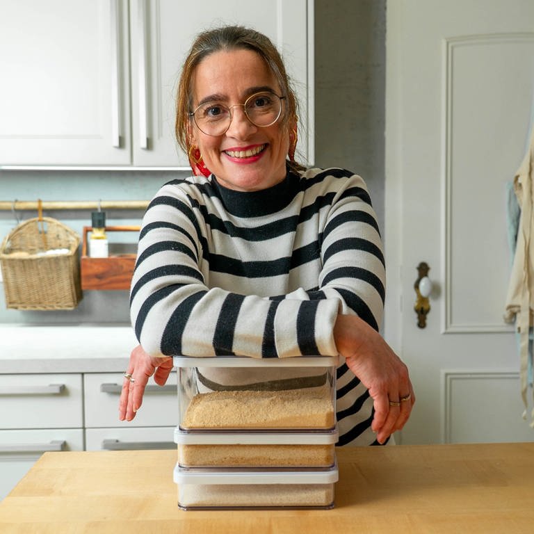Junge Frau mit Brille und gestreiftem Pullover lehnt über einem Stapel von Büchern in der Küche