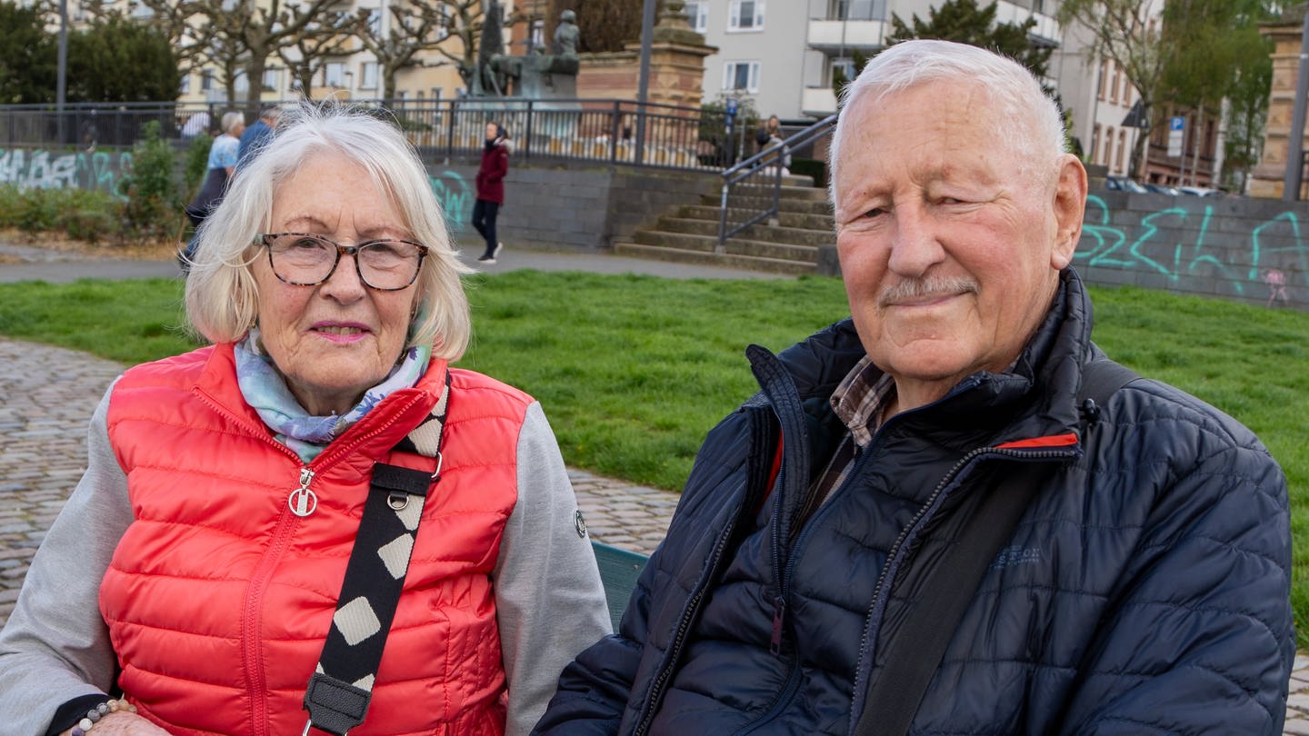 Eine ältere Dame mit Brille und pinker Jacke und ein älterer Herr mit dunkler Jacke sitzen auf einer Bank und schauen in die Kamera. (Foto: SWR)