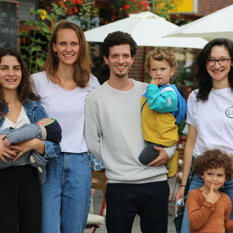 Vier Erwachsene und drei Kinder lächelnd vor einem Restaurant-Außenbereich.