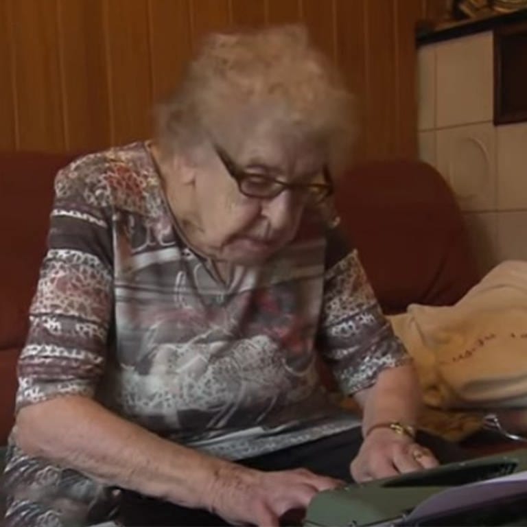 Alte Frau sitzt gebeugt über Schreibmaschine