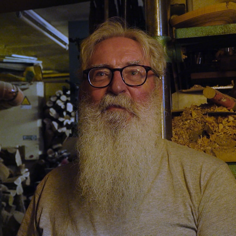 Ein älterer Mann mit Brille und langem weißen Bart steht vor Holzregalen in einem Schuppen (Foto: SWR)