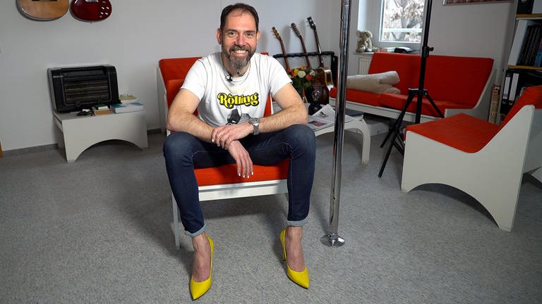 Mann sitzt in Zimmer mit gelben Highheels an den Füßen