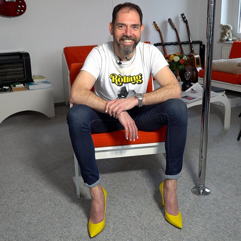 Mann sitzt in Zimmer mit gelben Highheels an den Füßen