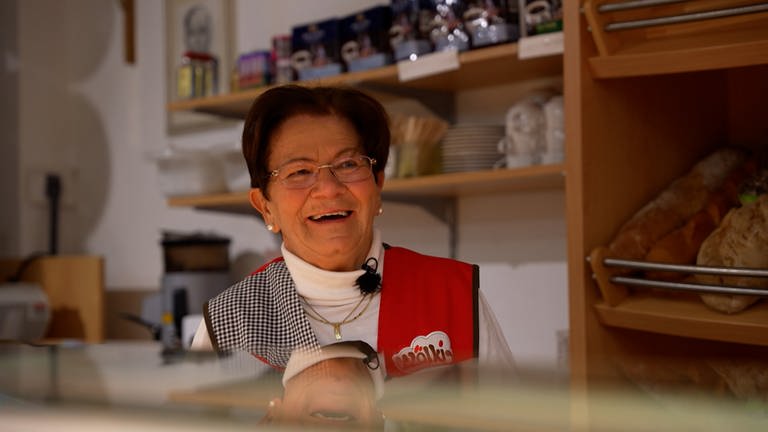 Gerda steht in ihrem Dorfladen und lächelt, hinter hier liegen Brötchen und Brot im Regal.  (Foto: SWR)