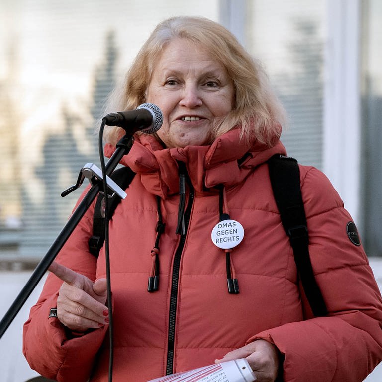 Die Gründerin von „Omas gegen Rechts” Anna Ohnweiler ist bei einer Demonstration und steht auf einer Bühne. Sie steht an einem Mikrofon und schaut in die Kamera.