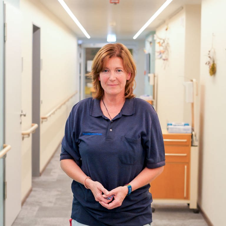 Heike ist Palliativkrankenschwester und steht in der Mitte eines hellen Flurs des Hospizes, neben ihr steht ein Strauß mit lila Tulpen.  (Foto: SWR)