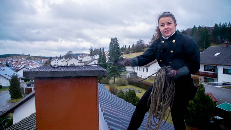 Schornsteinfegerin Janina steht auf einem Dach und reinigt den Schornstein. (Foto: SWR)