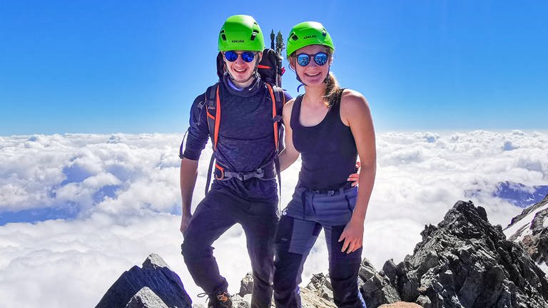 Zwanzigjähirger Frau und Mann stehen mit Wanderausrüstung auf dem Gipfel eines Berges.  (Foto: Keine)