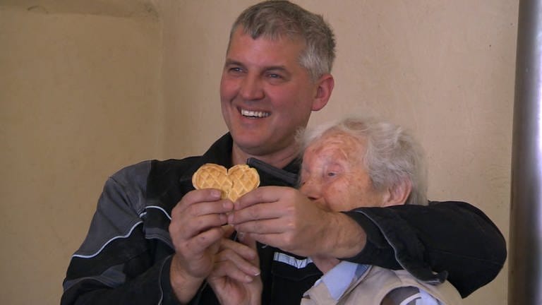 Ein Mann und eine Seniorin halten ein Waffel-Herz in der Hand und lächeln (Foto: SWR)