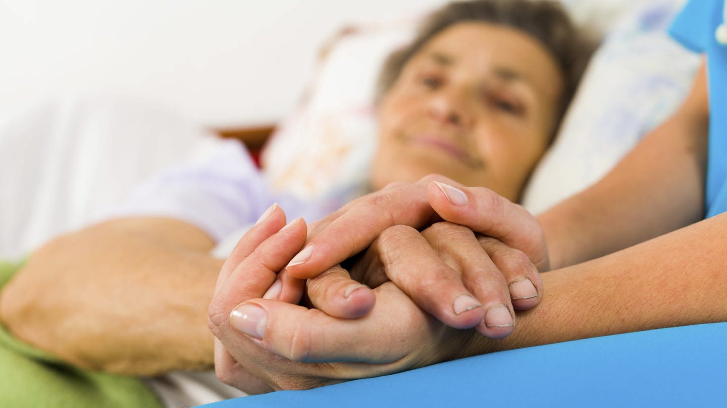 Eine Krankenschwester hält die Hand einer älteren Frau (Foto: Getty Images)