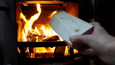 Jemand gibt einen Holzscheit in einen brennenden Kaminofen (Foto: dpa Bildfunk, Picture Alliance)