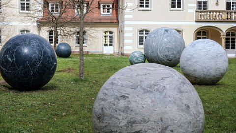 Steinerne Kugeln aus unterschiedlich farbigen Gesteinen und in verschiedenen Größen liegen als Ensemble in einem Gartenstück des Heidelberger Kunstvereins. (Foto: Verein der Freunde und Förderer des Skulpturenparks Heidelberg e. V.)
