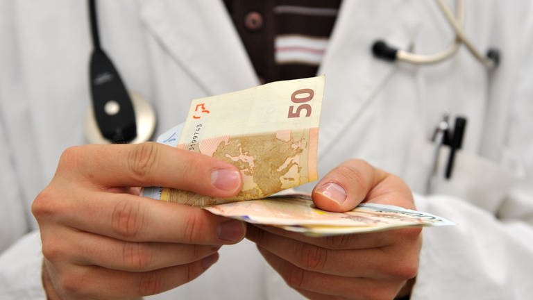 Ein Mann im Arztkittel zählt Geldscheine