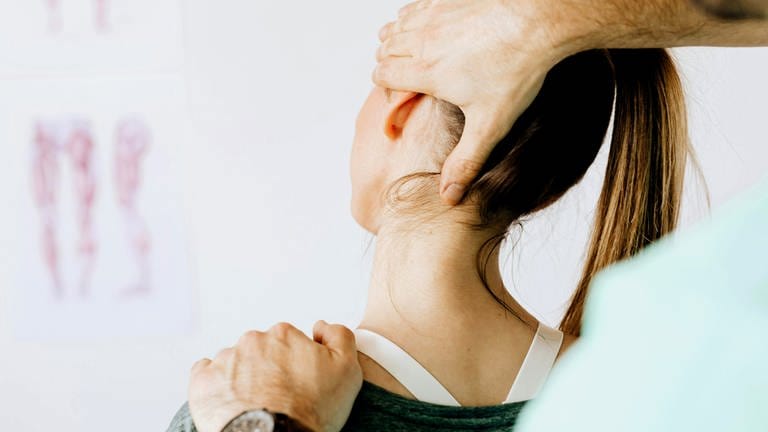 Physiotherapeut hält Kopf und Nacken einer Frau mit beiden Händen