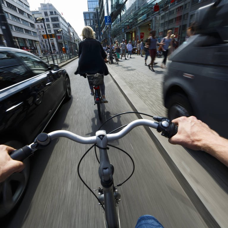 #besserRadfahren: Ein Radfahrer wird im Stadtverkehr von einem nah vorbeifahrenden Auto überholt. (Foto: IMAGO, imago/photothek)