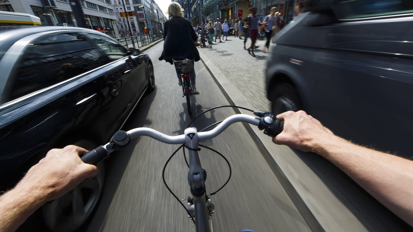 #besserRadfahren: Ein Radfahrer wird im Stadtverkehr von einem nah vorbeifahrenden Auto überholt. (Foto: IMAGO, imago/photothek)