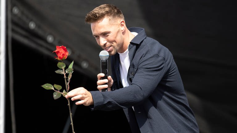 Ramon Roselly steht auf der Bühne und hält eine rote Rose in der Hand.
