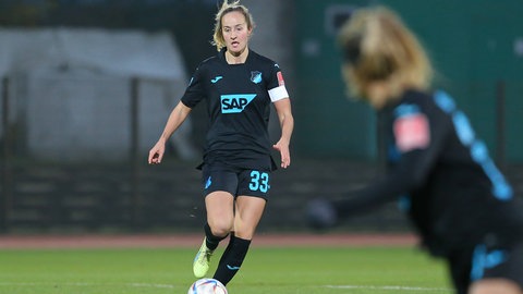 Fabienne Dongus im dunkelblauen Trikot der TSG Hoffenheim läuft mit dem Ball am Fuß auf die Kamera zu. Am rechten Bildrand steht (unscharf) eine Mitspielerin.