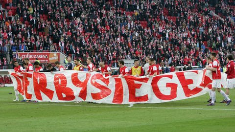 Spieler von Mainz 05 tragen nach dem Sieg gegen Kaiserslautern im Februar 2012 ein Banner in die Fankurve auf dem in roter Schrift auf weißem Grund "Derbysieger" steht.