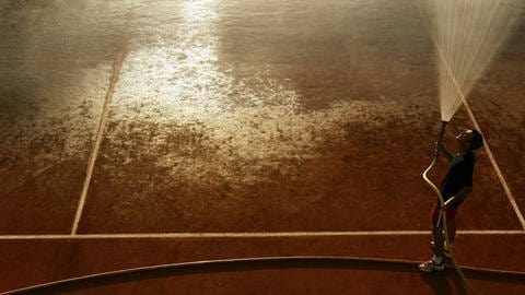 Mann sprüht Wasser auf einen Tennisplatz (Foto: IMAGO, IMAGO / Claus Bergmann)