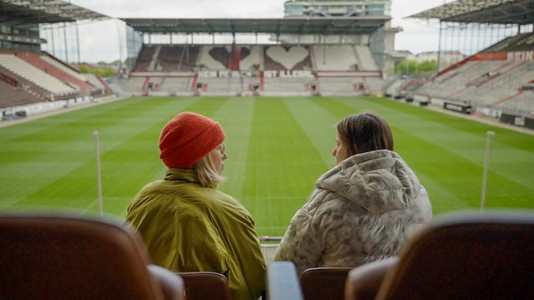 Zwei Frauen sprechen in einem leeren Stadion miteinander.