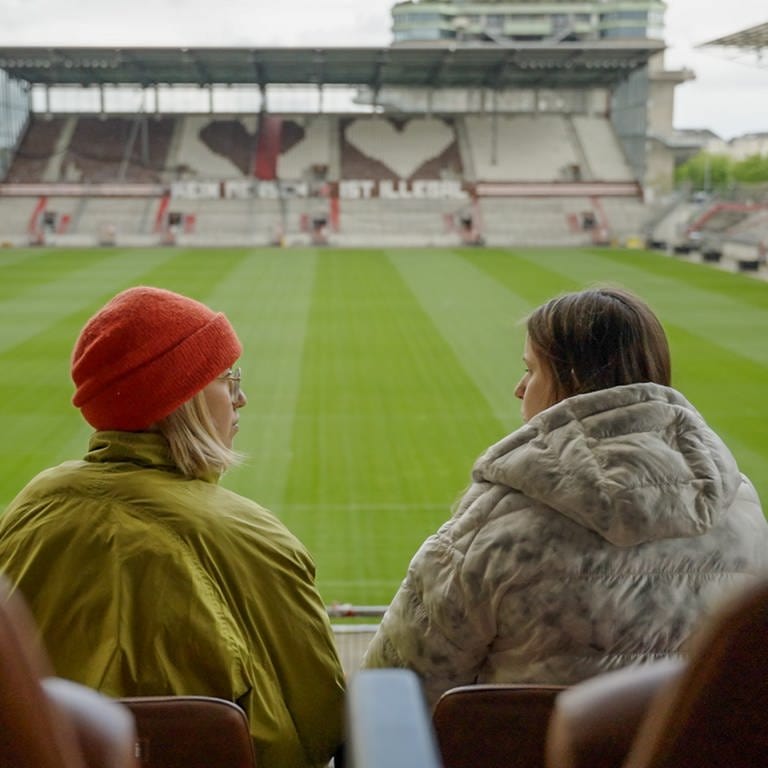 Zwei Frauen sprechen in einem leeren Stadion miteinander.