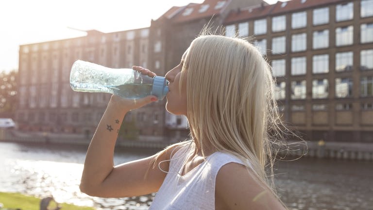 Frau trinkt beim Sport in der Hitze aus einer Wasserflasche