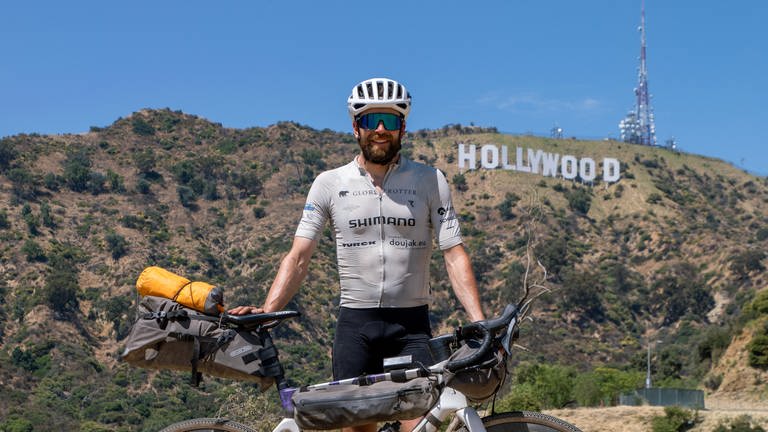 Jonas Deichmann steht mit seinem Fahrrad vor der Kulisse der Hollywood Hills in den USA (Foto: picture-alliance / Reportdienste, Picture Alliance)